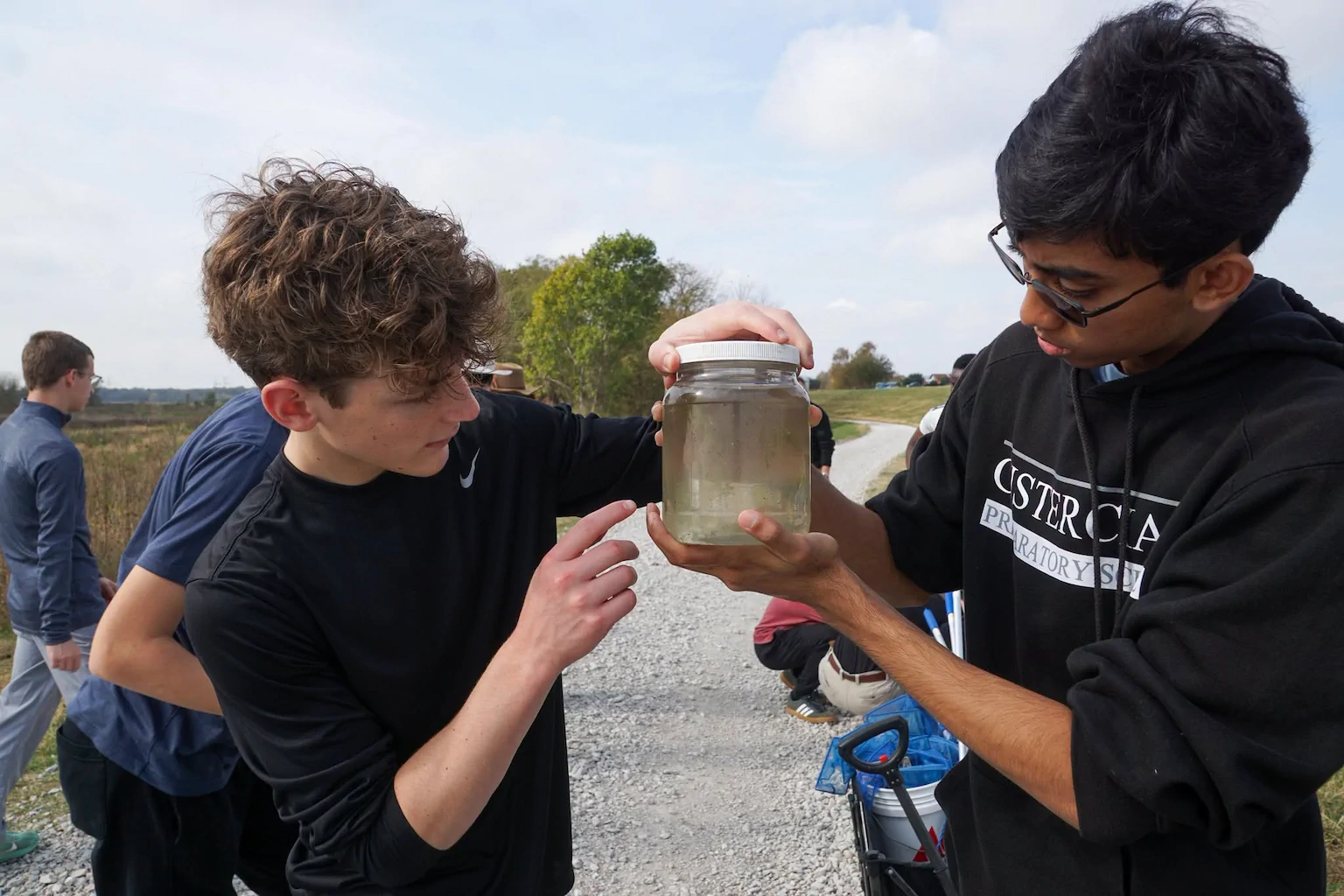 Two students examine a jar of pond water collected during an outdoor science investigation.
